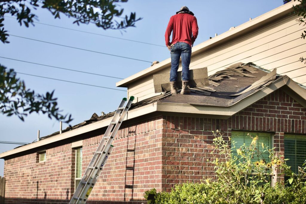 Man standing on a damaged roof of a home.